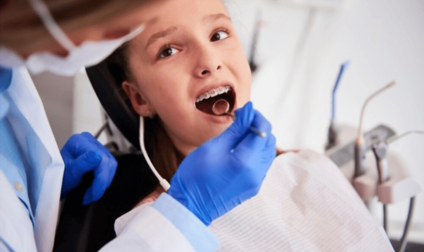 Op de afbeelding ziet u een jong patiënt in de behandelstoel met een beugel terwijl een tandarts met mondspiegel en tang het gebit nauwkeurig inspecteert. Dit beeld sluit naadloos aan bij Dental Delft Junior, waar gespecialiseerde kindertandheelkunde en orthodontische zorg centraal staan. De moderne praktijkinrichting en professionele instrumenten benadrukken de combinatie van mondzorg, esthetische tandheelkunde en grondige gebitsverzorging. Zo maakt deze opname direct duidelijk dat Dental Delft Junior staat voor hoogwaardige, kindvriendelijke tandartszorg in Delft.